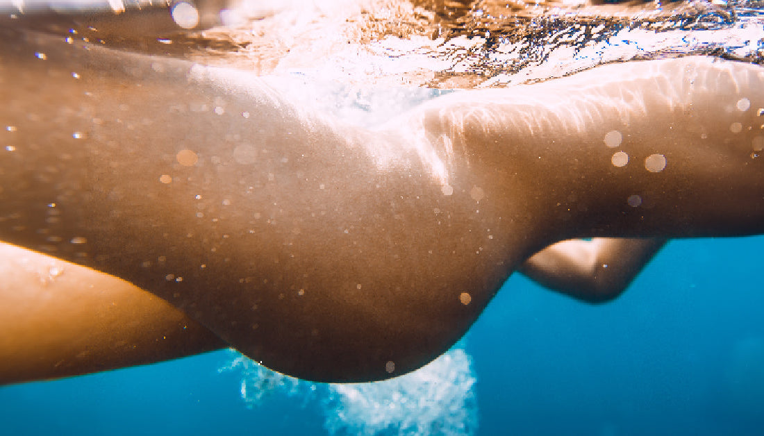 Underwater view of a person swimming with sunlight filtering through the water.